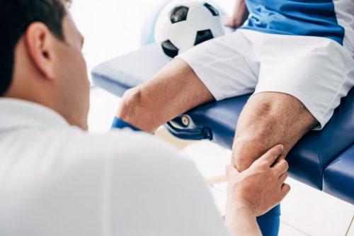 Partial,View,Of,Physiotherapist,Massaging,Leg,Of,Football,Player,In